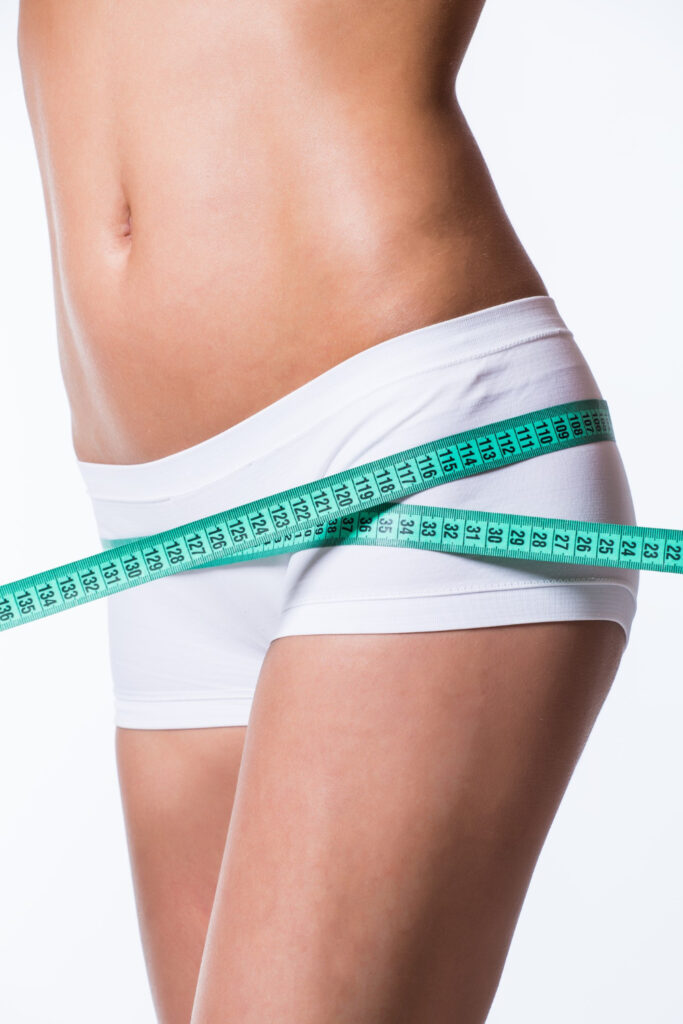 Cinta métrica verde rodeando la cadera y abdomen de una mujer, imagen asociada a la medición y contorneado corporal tras una abdominoplastia