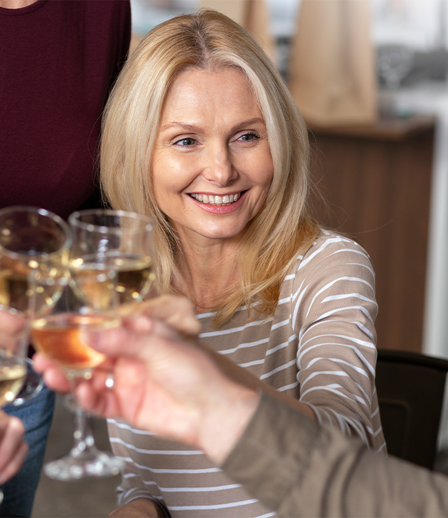 Mujer madura sonriente con mirada luminosa y descansada brindando con copa de vino, imagen representativa de bienestar tras una blefaroplastia