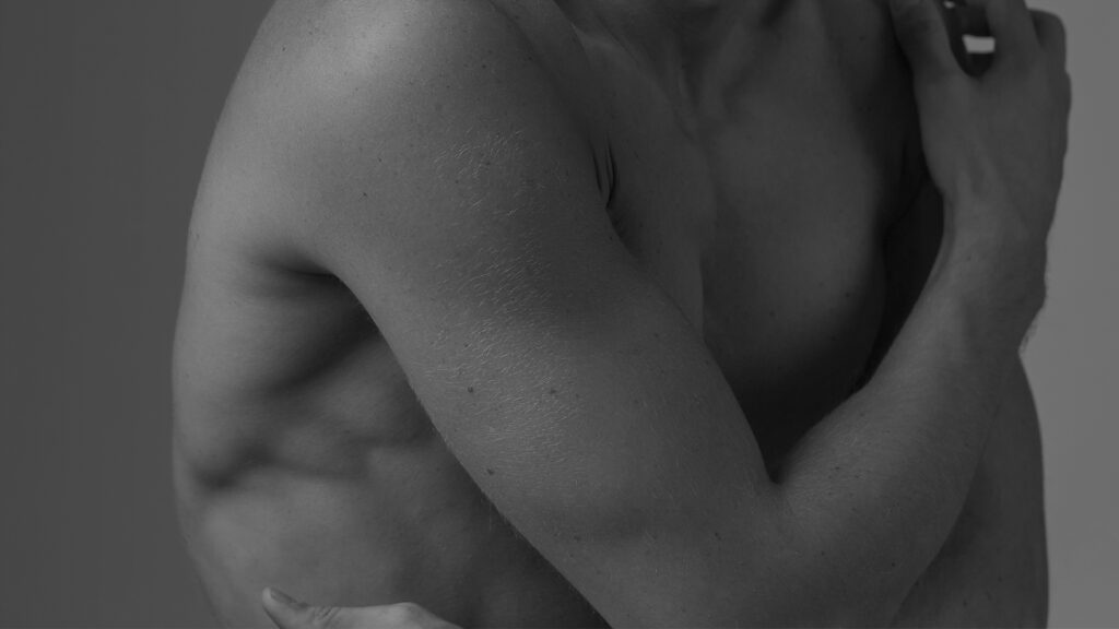 Primer plano artístico en blanco y negro del torso y brazo masculino, imagen evocadora asociada a cirugía corporal para hombres