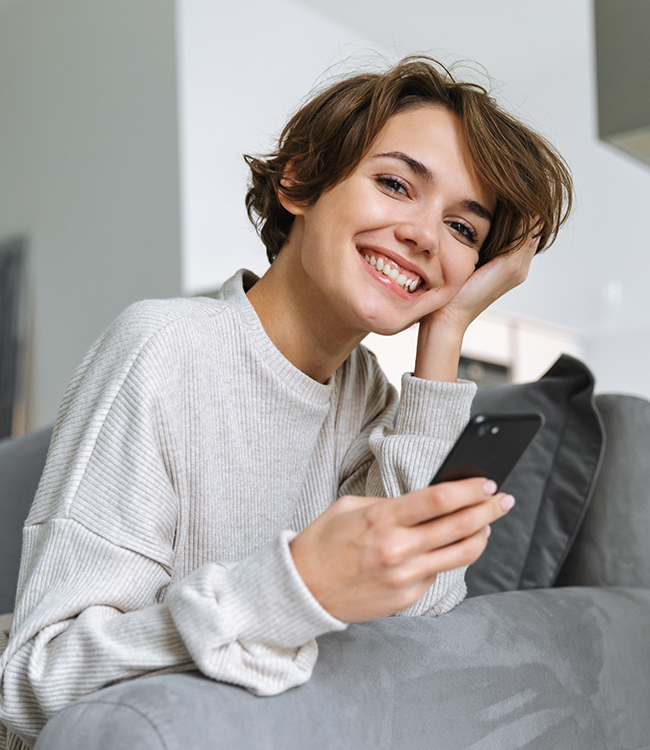 Mujer joven sonriente con nariz estilizada y rasgos armoniosos sosteniendo un móvil, imagen representativa de resultados de rinoplastia ultrasónica